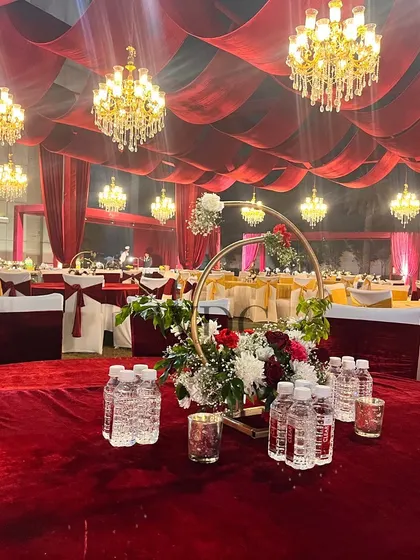 The guest dining area, with tables covered in luxurious red velvet and topped with floral ring centerpieces. The entire space is lit by numerous hanging chandeliers, creating a grand and opulent feel.