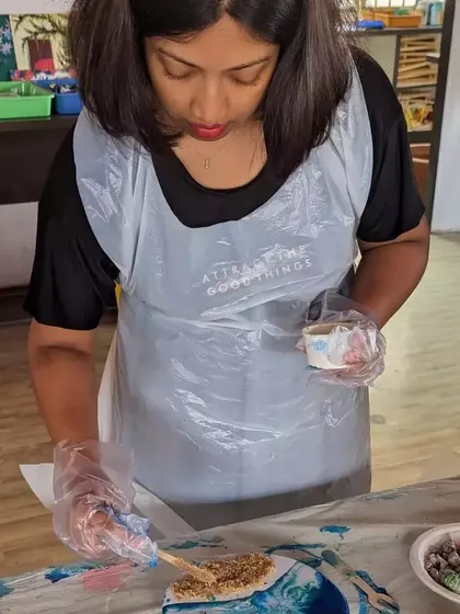 A participant carefully adding sand to her resin beach art, a step that brings a realistic, tactile element to the piece.