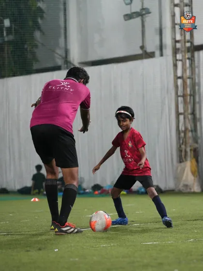 A coach provides one-on-one guidance to a young player, correcting her stance and technique to improve her dribbling skills.