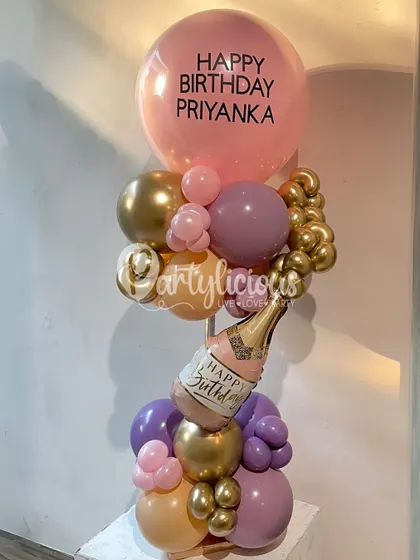A chic and celebratory birthday balloon bouquet in shades of peach, purple, and gold, complete with a mini champagne bottle balloon.