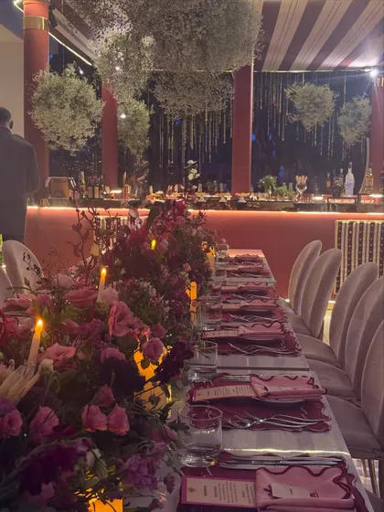 A finale dinner designed to celebrate two families becoming one. The tables are adorned with lush pink and red floral arrangements and candlelight, creating a warm and romantic atmosphere.