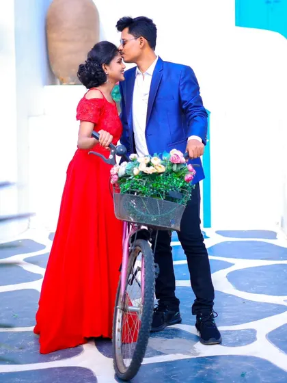 A sweet pre-wedding moment with a bicycle prop full of flowers. The Santorini-style background adds a fresh and romantic feel.