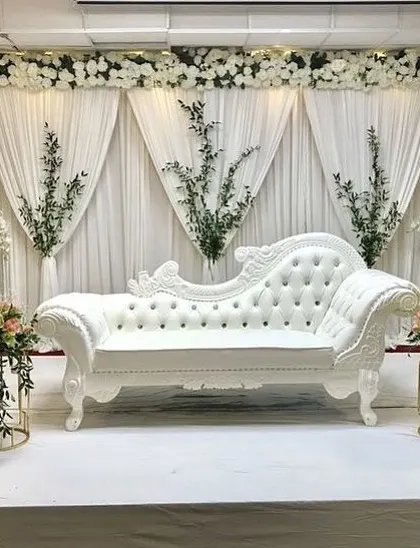 An all-white stage for a Nikah ceremony or elegant reception. The clean white draping, classic furniture, and simple green accents create a look of pure sophistication.