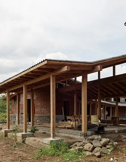The farmhouse in Kamshet is defined by its long, covered verandas supported by a timber frame structure. These spaces provide shelter from the sun and rain while maintaining a constant connection to the surrounding landscape.