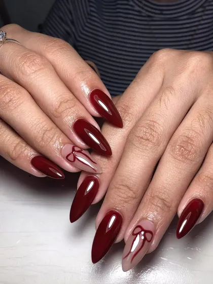 A dramatic, long stiletto set in deep red with delicate bow line art on accent nails. This is a perfect blend of bold color and feminine detail.