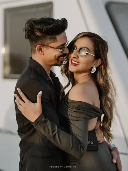 A close, romantic embrace between the couple, their stylish sunglasses and loving smiles capturing the essence of their chic desert engagement session.