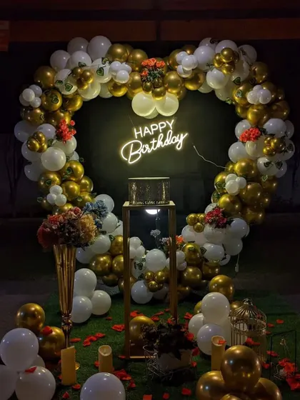 A heart-shaped balloon arch made of gold and white balloons, with a neon "Happy Birthday" sign. This setup is perfect for a glamorous and romantic celebration at night.
