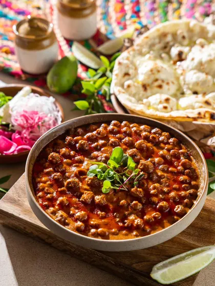 A bowl of chana masala served with fresh garnishes and naan. The bright, airy lighting makes this classic North Indian dish look fresh and appealing.
