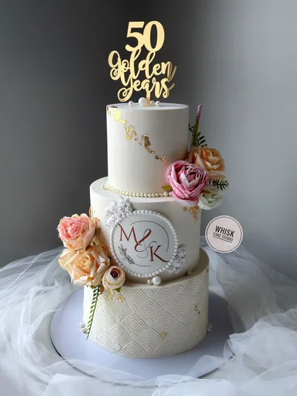 A golden anniversary cake fit for 50 years of love. This three-tiered masterpiece features a custom monogram, elegant textures, and beautiful handcrafted flowers.