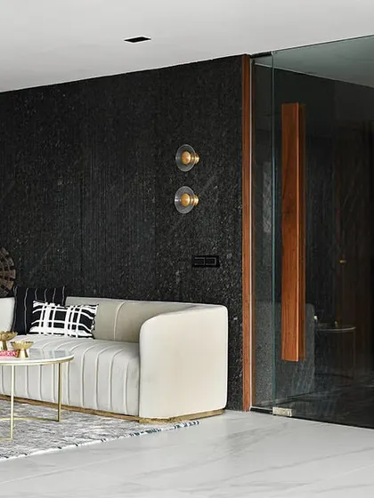 The waiting area combines a plush cream sofa with a dramatic black stone wall, creating a sophisticated study in contrast.