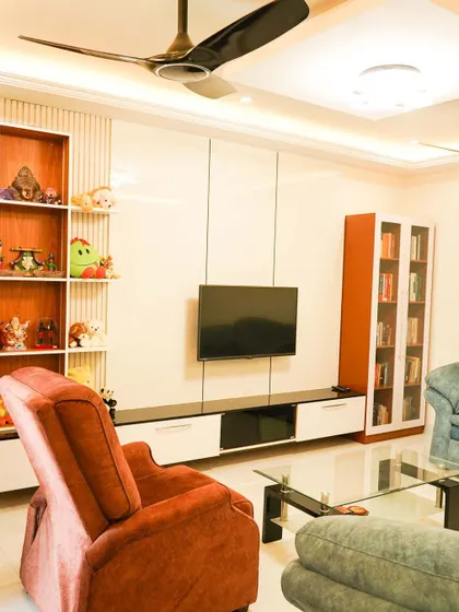 This living room combines comfort with style, featuring a plush recliner sofa and a sleek, wall-mounted TV unit with integrated shelving for display and storage. The high-gloss finish adds a touch of modern elegance.