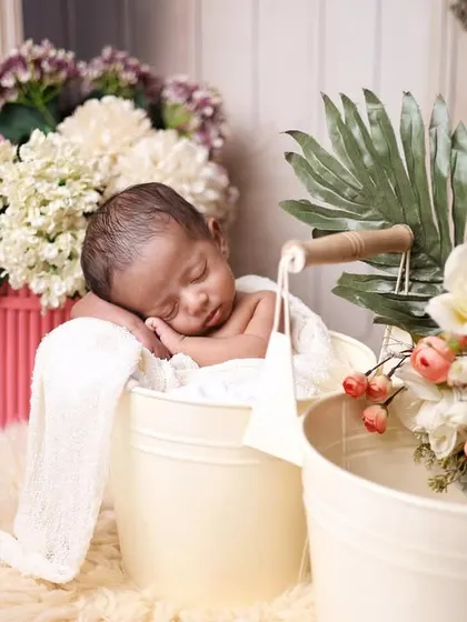 A newborn sleeping in a bucket, surrounded by a beautiful arrangement of flowers. This setup combines rustic charm with floral elegance.