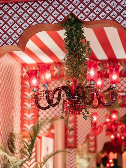 A close-up of a red chandelier with green vines, set against a red and white striped canopy, showcasing the attention to detail.