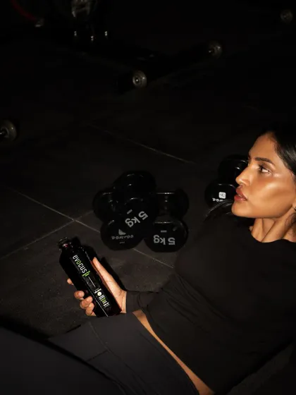 Staying hydrated is key, especially during a tough workout. Here I am taking a break with some black alkaline water, surrounded by dumbbells.