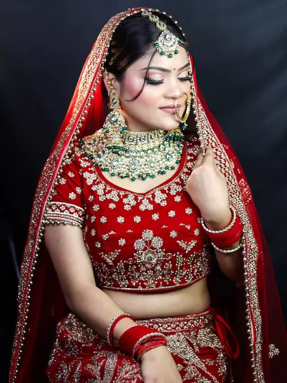 The full bridal look, showcasing the rich red lehenga and emerald jewelry. We teach how to select makeup tones that complement the bride's attire and jewels.