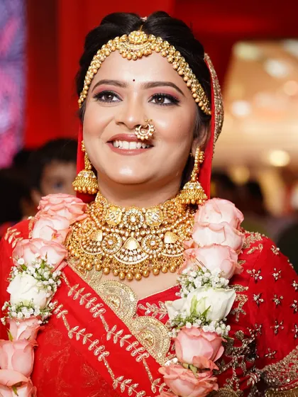 A smiling bride looking radiant. Her look features a classic gold choker and matching jhumkas, paired with a floral garland.