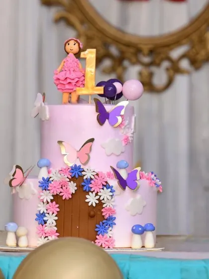 A charming two-tiered fairy house cake, complete with a tiny door, mushrooms, and beautiful flowers. A fondant fairy and butterflies complete this magical scene.