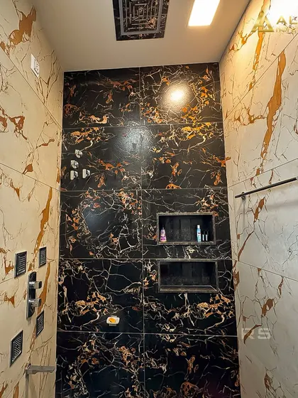 The shower area in the black and gold marble bathroom, featuring a modern shower panel and built-in storage niches. The design is both opulent and practical.