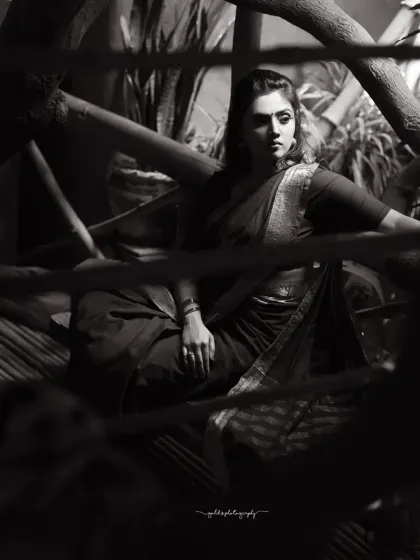 A moody black and white portrait of a model in a saree, framed by wooden structures. The shadows and light create a cinematic and emotional atmosphere.