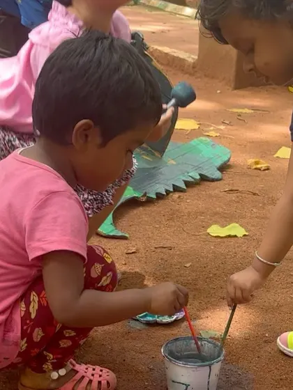 A young artist painting a wooden dinosaur cutout during an outdoor event. We often bring different materials and objects for children to paint, moving beyond traditional canvases.