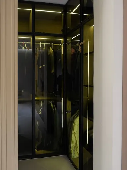 A peek inside the walk-in closet, featuring black-framed glass doors and internal lighting. This design keeps clothes organized and visible while feeling like a high-end boutique.
