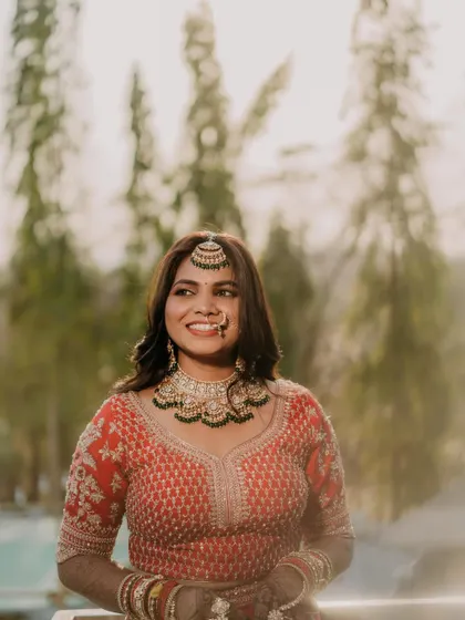 A stunning outdoor portrait where the natural light makes her skin glow. The makeup is glamorous yet soft, perfectly complementing her red lehenga and the beautiful decor.