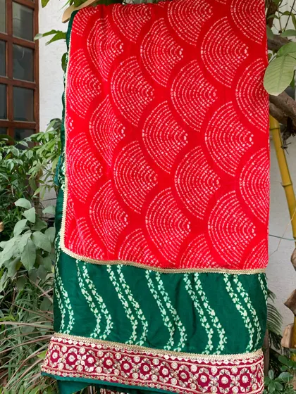 The vibrant red bandhani dupatta provides a stunning contrast to the green lehenga.