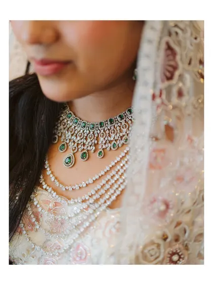 A stunning close-up of the bride's layered diamond and emerald necklace. This shot captures the luxury and intricate beauty of her wedding jewelry.
