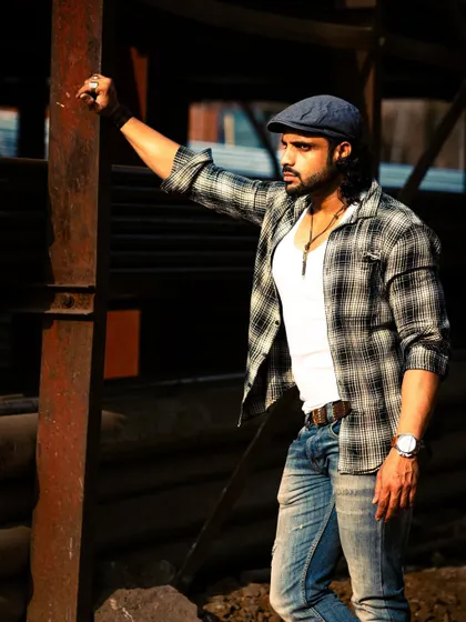 A different look in the same industrial setting. The plaid shirt and cap give off a more casual, rustic vibe against the metal structures.