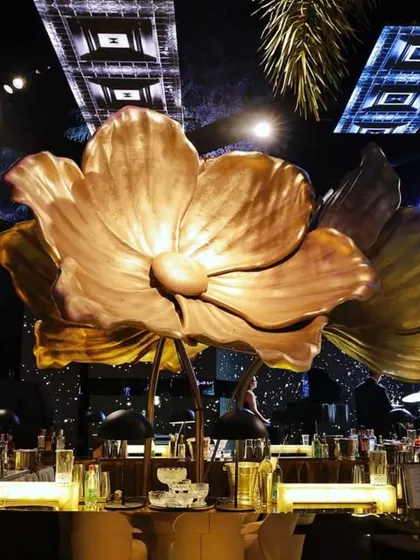 The giant golden flower sculpture seen from the front, with the bar and stage lights creating a dynamic and colorful backdrop.