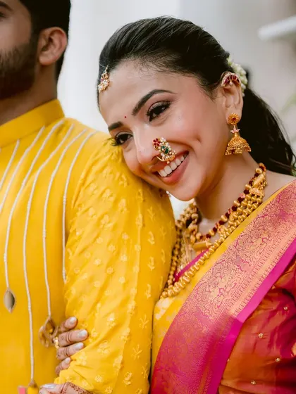 A candid moment of happiness. This close-up shows the radiant, skin-like finish of the makeup, with a soft smile that lights up her face. The traditional Maharashtrian jewelry and bright yellow saree complete this joyful bridal look.