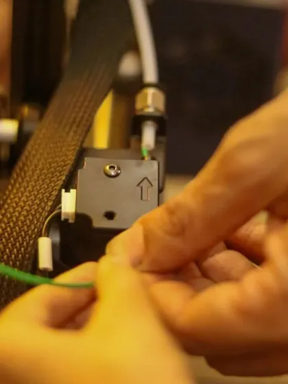 A close-up of hands feeding filament into a 3D printer's extruder. This is the first step in bringing a digital design into the physical world.