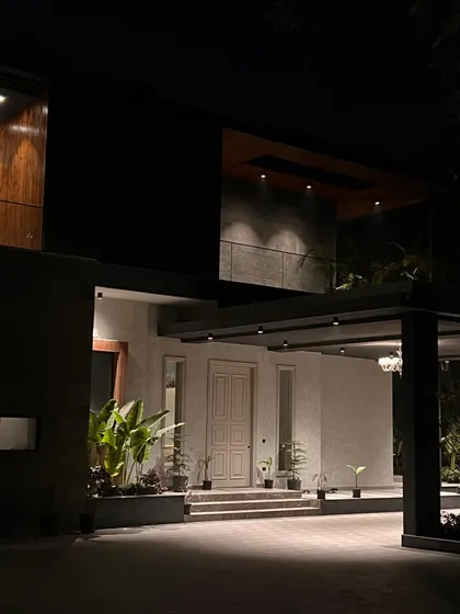 The entrance of "The One" residence is dramatic and welcoming after dark. Strategic lighting accentuates the large canopy, the texture of the walls, and the lush plants, guiding visitors toward the front door with a sense of quiet grandeur.