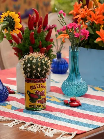 A tabletop arrangement featuring a cactus in a can, a striped table runner, and colorful vases, creating a fun and authentic Mexican feel.