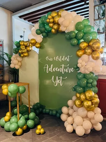 A chic and modern take on a jungle theme with the words "Our Wildest Adventure Yet." The olive green, white, and gold balloons create a stylish look.