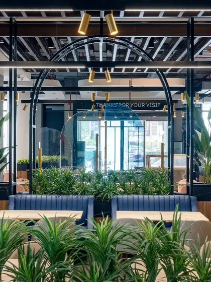 A view from the seating area at Haldiram's looks out towards the entrance. The design uses lush greenery and warm walnut-cherry finishes to create a welcoming atmosphere that invites engagement.