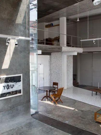 The interior of the Artrovert studio, featuring raw concrete surfaces, double-height volumes, and a mezzanine study. The space is designed to be rugged, flexible, and filled with natural light.