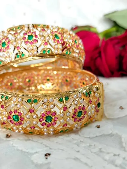 These openable Jadau kangans (bangles) are rich with detail, featuring pearls and floral motifs in red and green. This image captures their luxurious and traditional appeal.