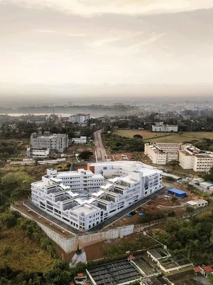 An aerial drone shot captures the full scale of the Manipal School of Architecture & Planning (MSAP) on its contoured site. The building's fragmented form creates a series of courtyards and open spaces, breaking down the monolithic scale.