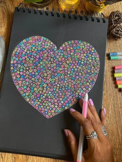 A heart shape filled with thousands of tiny, colorful flowers, created with gel pens on black paper.