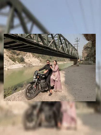 An artistic shot with a blurred foreground, drawing the viewer's eye to the couple posing on the motorcycle.