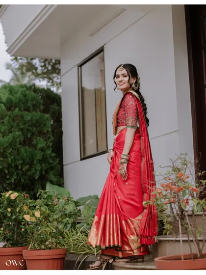 A full-length portrait of the bride in a garden setting, her red saree standing out against the green.