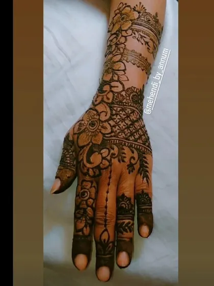 A detailed look at a fusion bridal design. This piece combines bold floral work on the arm with delicate hanging chains on the fingers and a cross-hatched net pattern on the back of the hand.