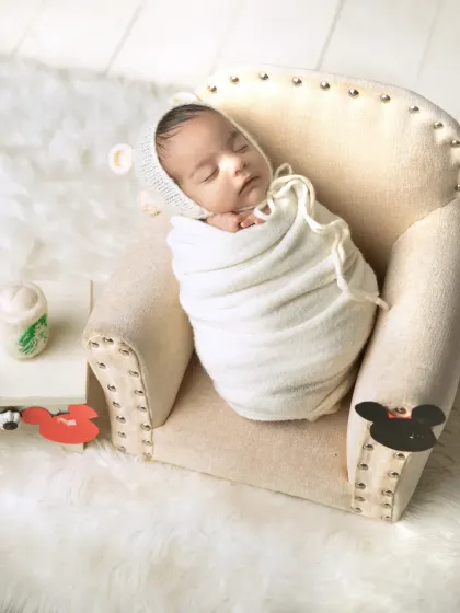 A wider shot of the swaddled baby in the armchair, showing a hint of a Mickey Mouse theme with the garland in the foreground.