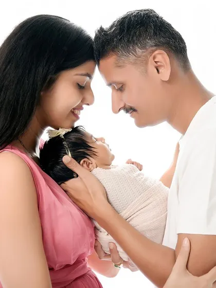A classic newborn and family portrait against a clean, white background. The parents' heads are touching as they hold their baby, creating a strong triangular composition that symbolizes family unity.