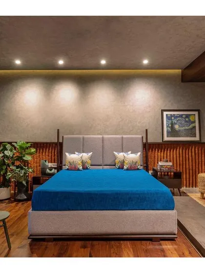 The master bedroom in "Between Two Trees" features a platform bed and a backdrop of textured walls and wood paneling. The design is minimal yet warm, creating a calming environment.