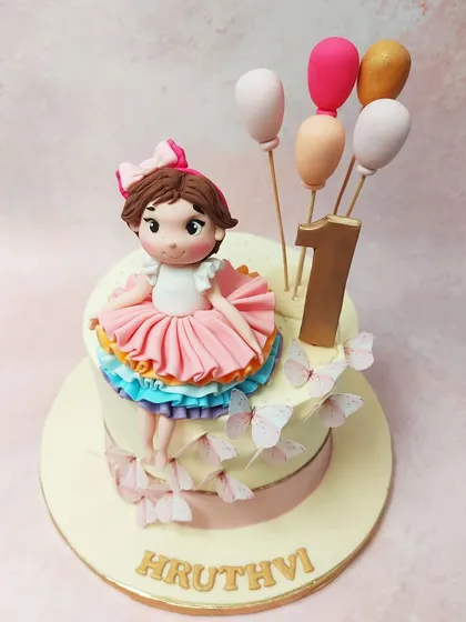 We celebrate a first birthday with this enchanting princess butterfly cake. A sweet fondant girl in a rainbow tutu sits atop the cake, which is adorned with fluttering butterflies and a bouquet of balloons, creating a scene of pure childhood magic.