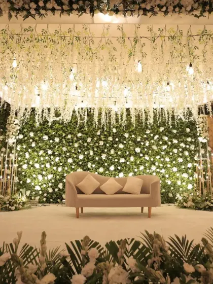 A straight-on shot of the elegant white floral stage, emphasizing the dense flower wall and the delicate hanging floral ceiling. This view showcases the sheer volume and artistry of the floral work involved.