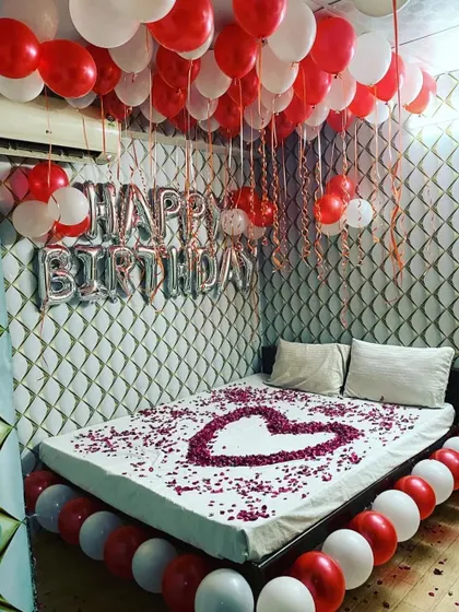 A classic romantic birthday surprise with a bed decorated with a heart made of rose petals, and red and white balloons filling the room.