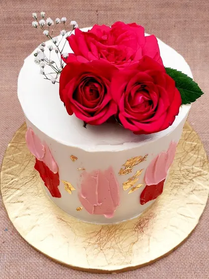 We celebrate romance with the classic beauty of red roses. Fresh, vibrant red roses sit atop a simple white cake, which is artfully decorated with abstract brushstrokes of red and pink buttercream and flecks of gold leaf for a modern, artistic touch.